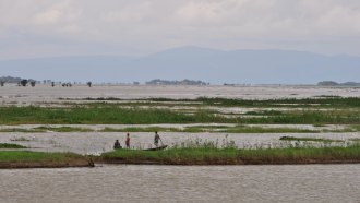 Three people on a boat look at the Ganges River with mountains in the background