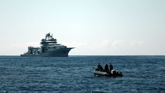 A photograph of the OceanXplorers ship in the background with crew members standing on an inflatable motorboat in the foreground